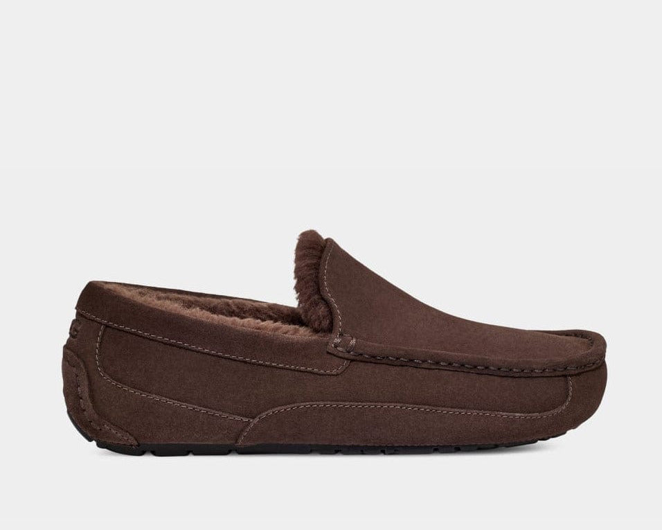 A UGG Ascot suede slipper in brown color with a rubber sole, featuring a sheepskin lining and a logo emboss.