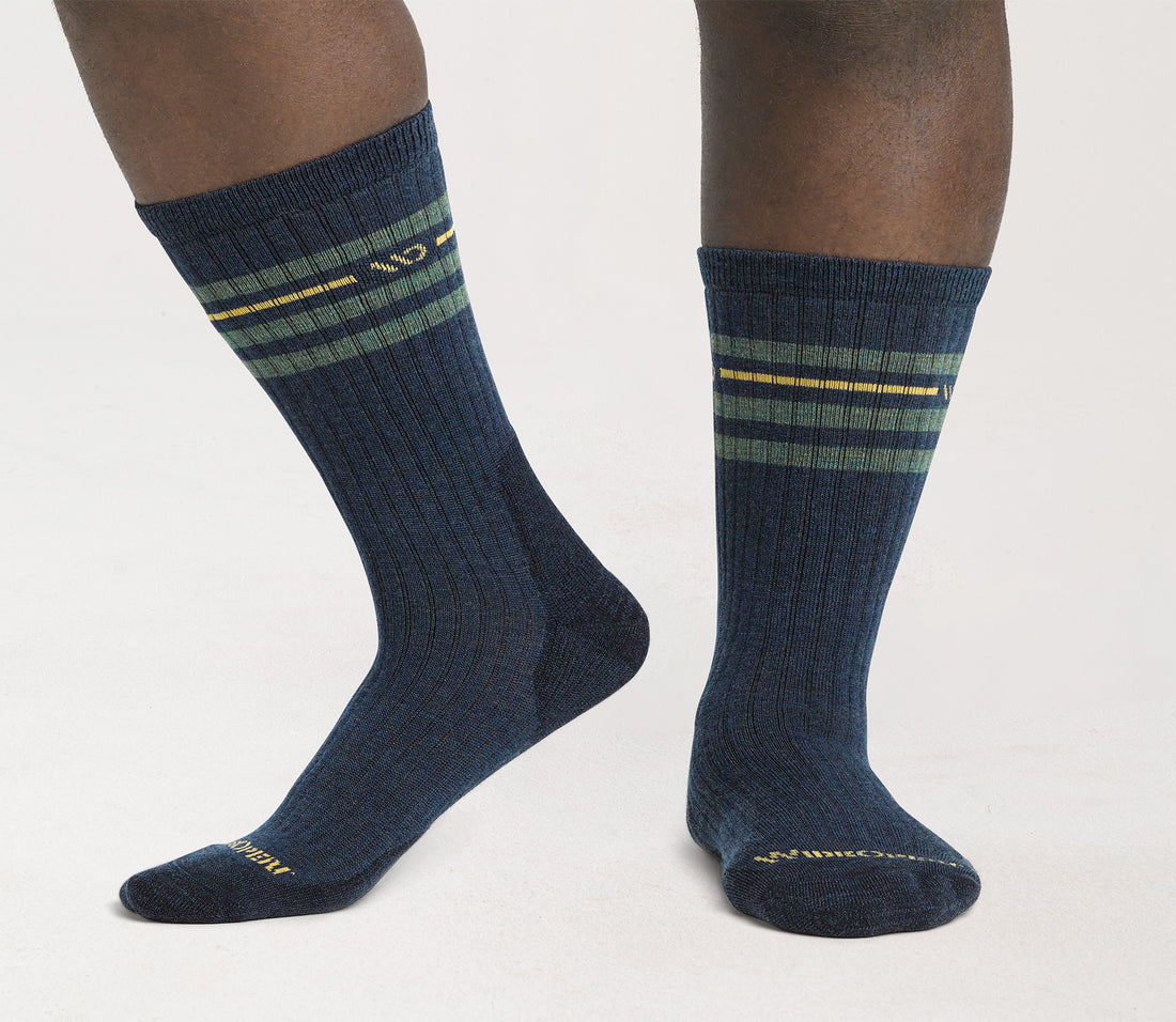 A pair of vintage stripe cushioned crew socks in denim blue color with yellow and green stripes, worn on a person's feet.