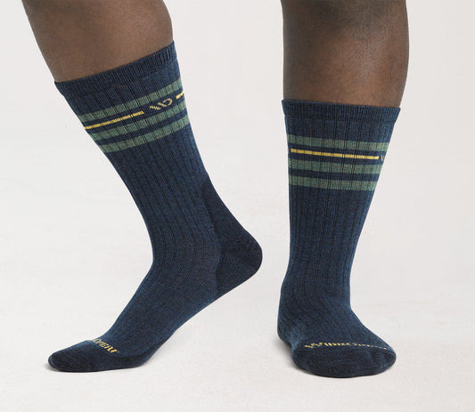 A pair of vintage stripe cushioned crew socks in denim blue color with yellow and green stripes, worn on a person's feet.