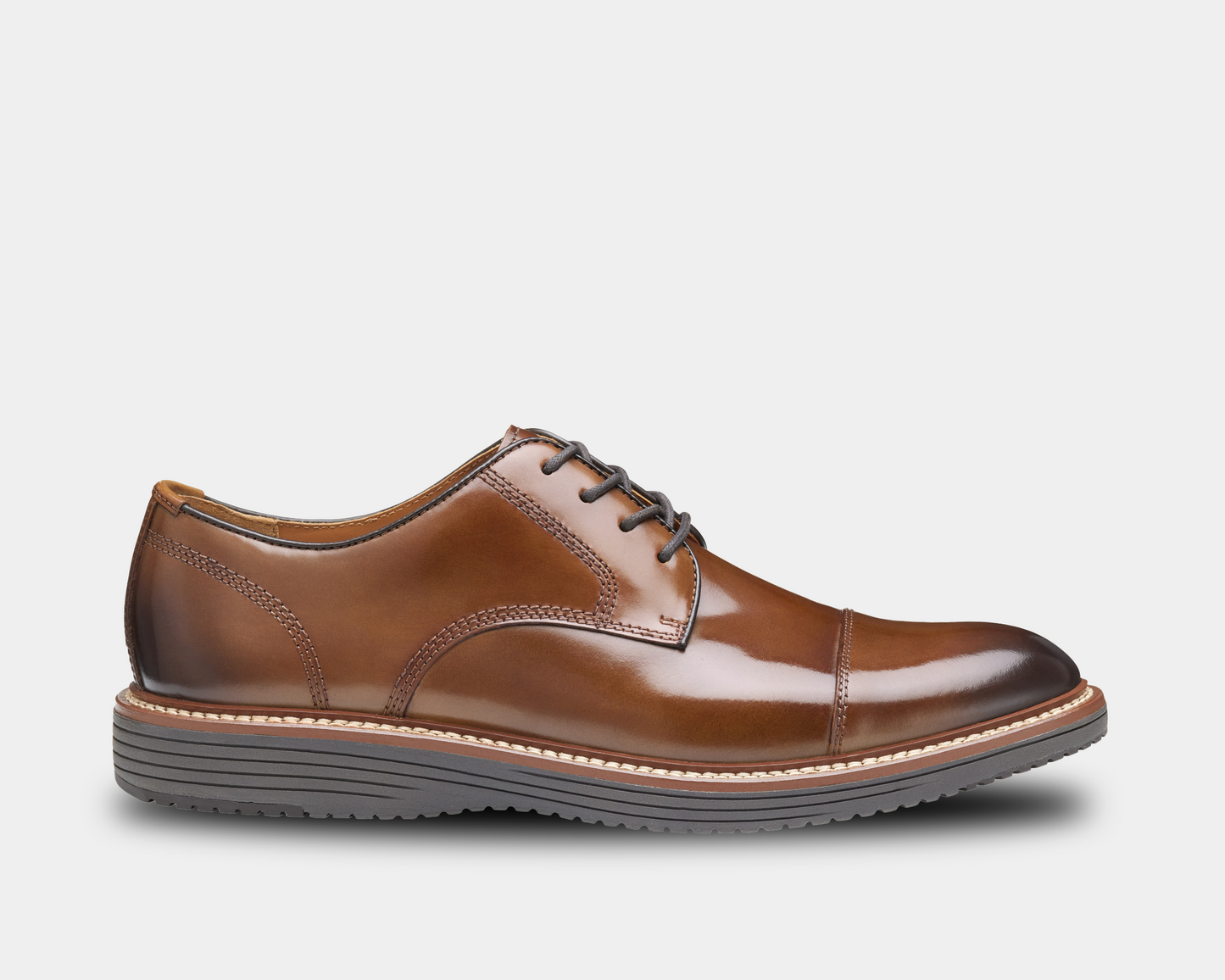 A tan full-grain leather cap toe Oxford shoe with a lace-up closure, featuring a flexible rubber sole and a low heel.